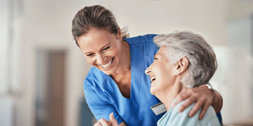 Smiling caregiver embracing elderly woman during in-home homemaking service.