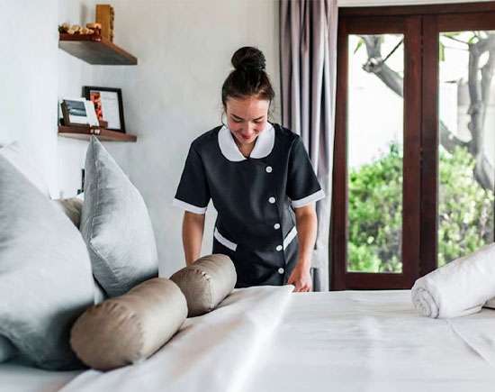 A caregiver making the bed in a client's room as part of homemaking services.