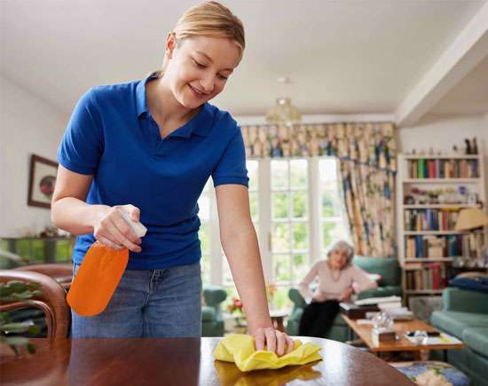 A caregiver cleaning a table as part of senior house cleaning services, ensuring a safe and tidy home for elderly individuals.