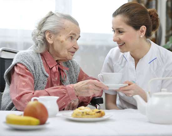 Caregiver helping senior woman with meal, reflecting the convenience and support of in-home meal prep for seniors, enhancing their overall well-being and independence.